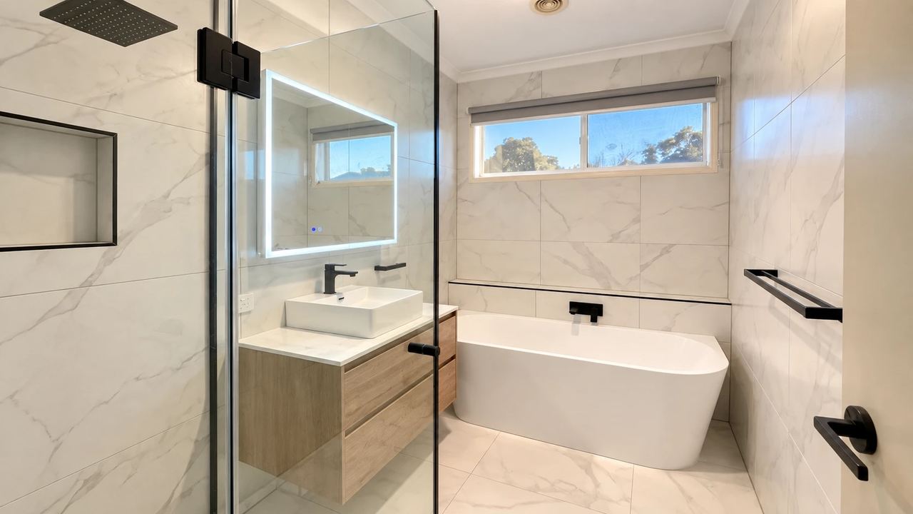Renovated bathroom in Cranbourne East with a frameless glass shower, freestanding bath, wall-hung timber vanity and illuminated mirror cabinet