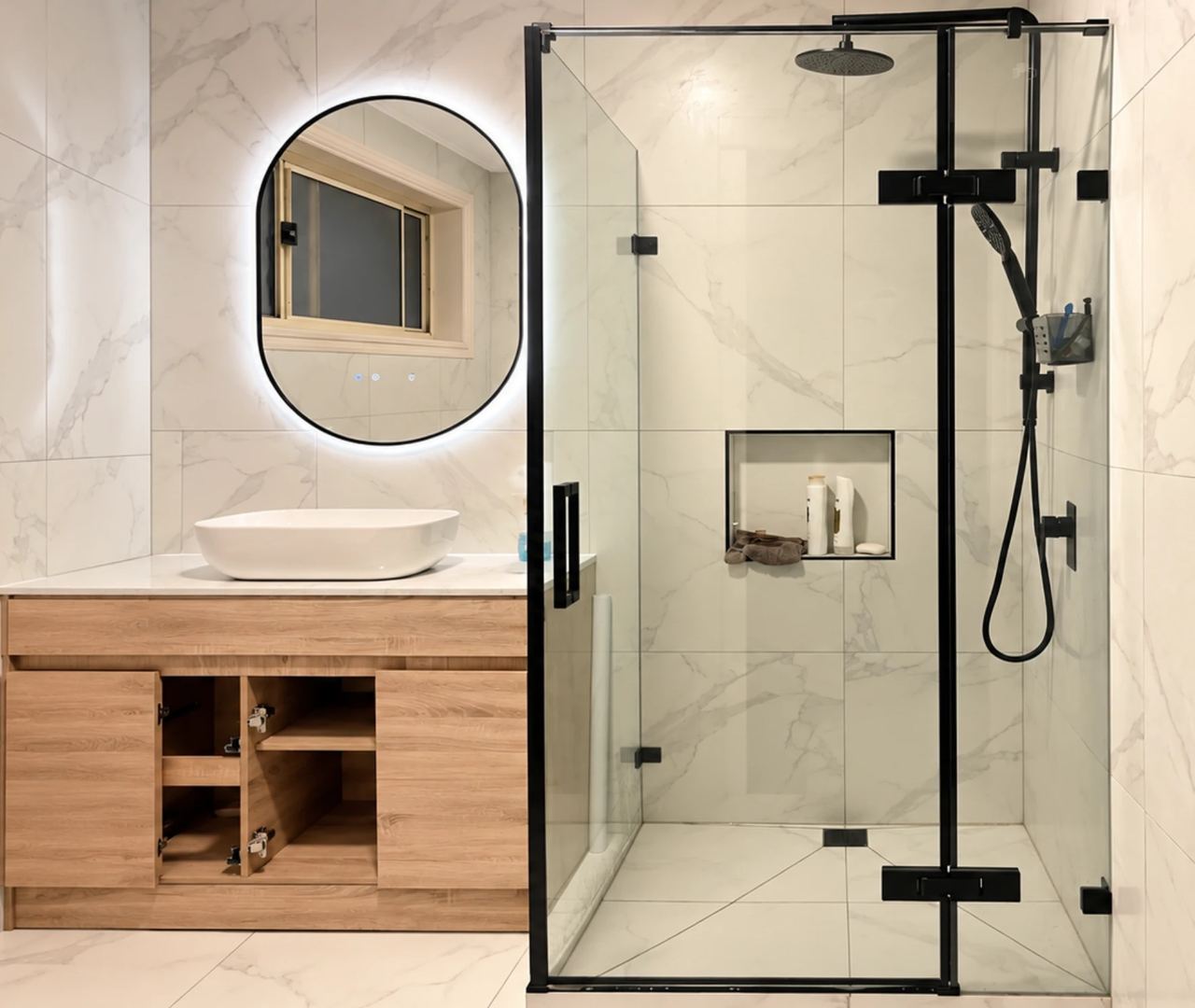 Renovated bathroom in Cranbourne North with a black-framed shower screen, backlit oval mirror and timber vanity