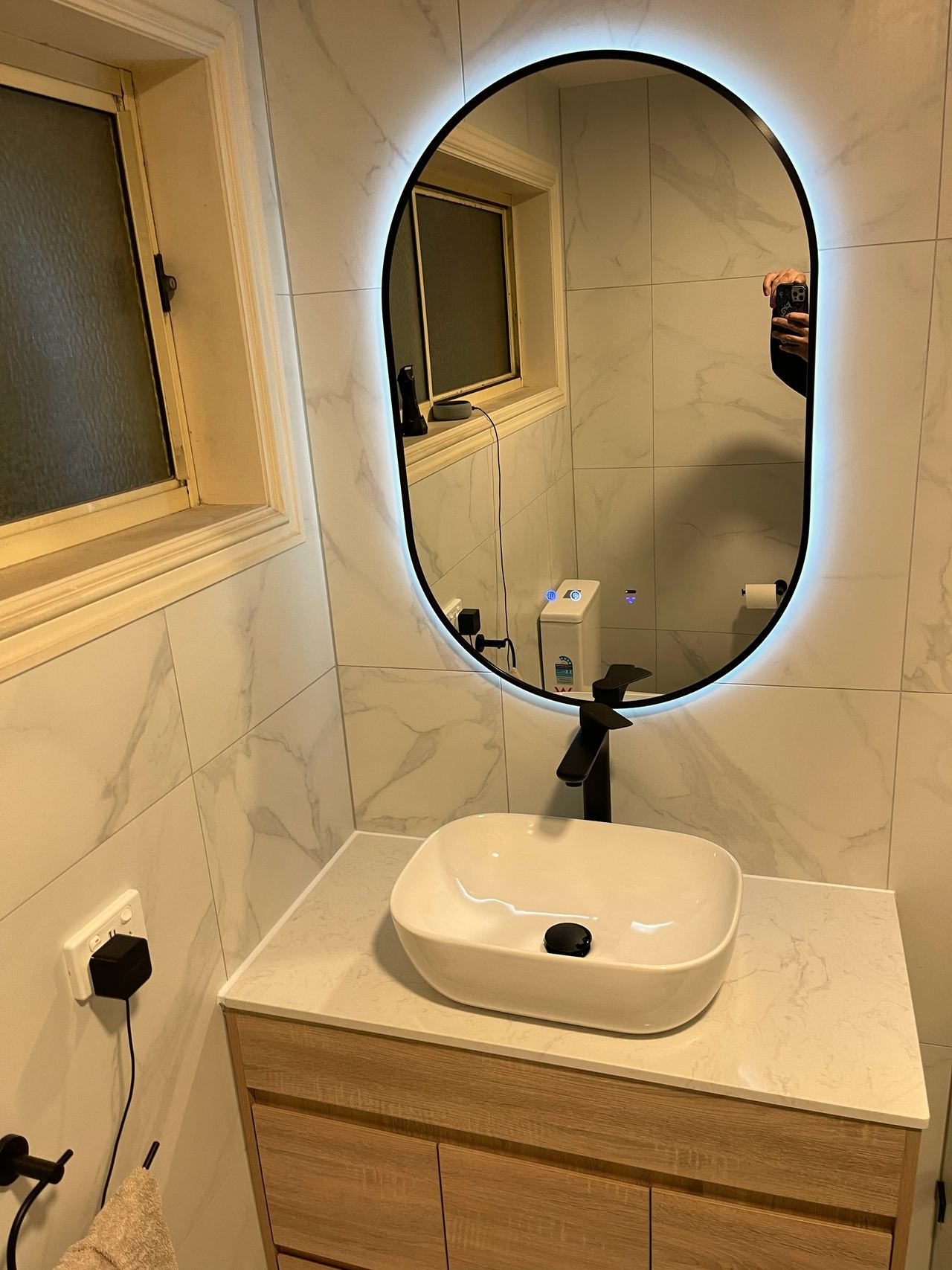 Renovated bathroom in Cranbourne North with a timber vanity, stone top, vessel basin and backlit oval mirror