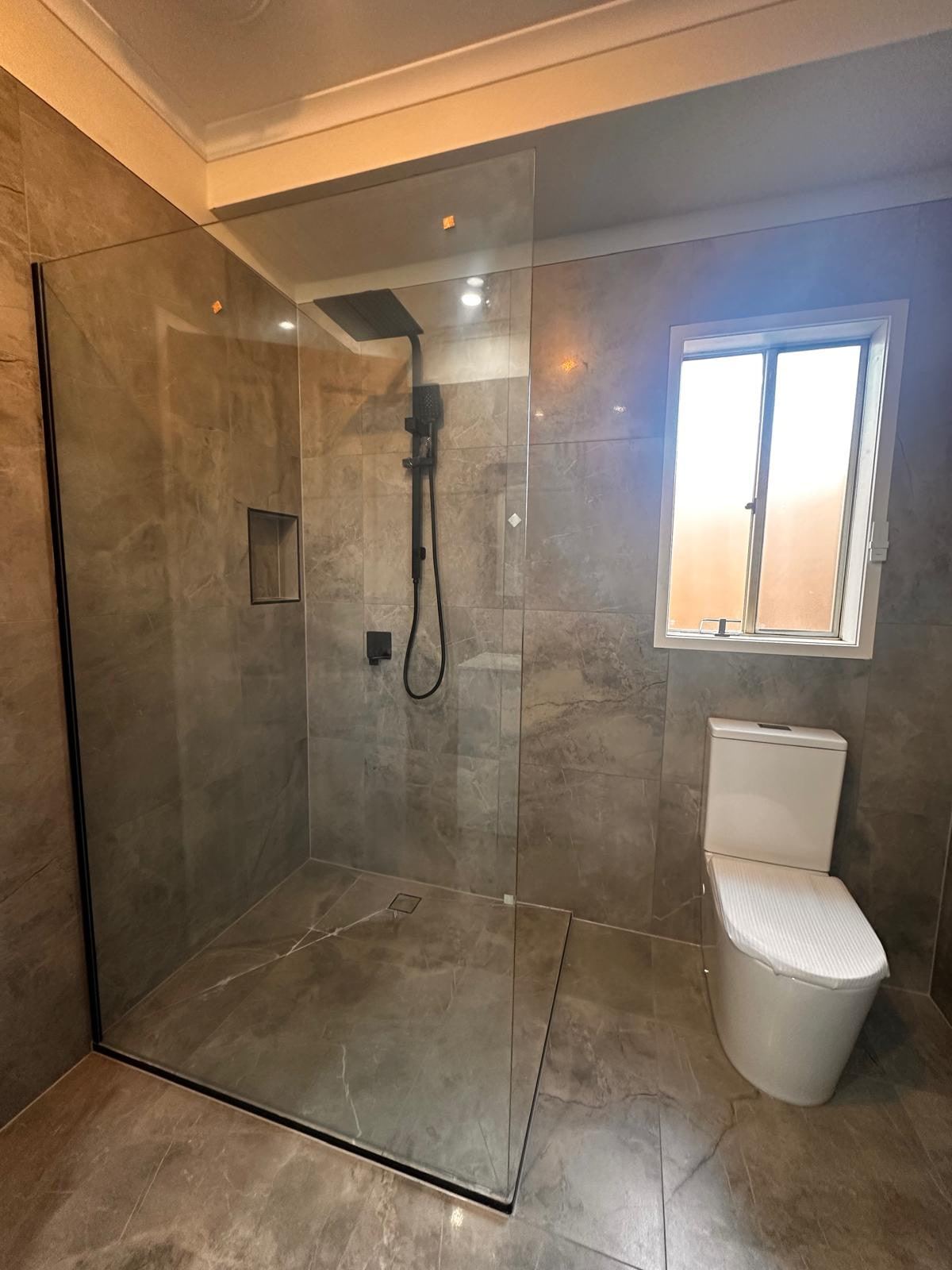 Renovated bathroom in Cranbourne West with a walk-in shower, black-trimmed glass panel and dark marble-look tiles