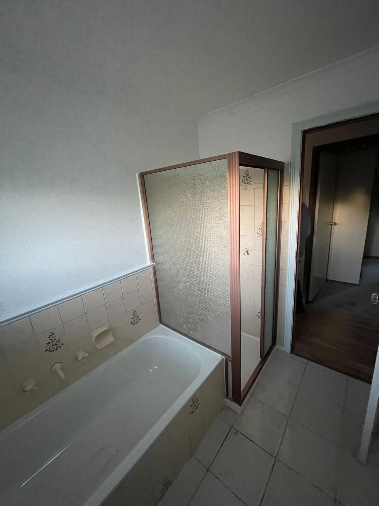 Before: original bathroom with a bath beside a framed shower and half-height wall tiles