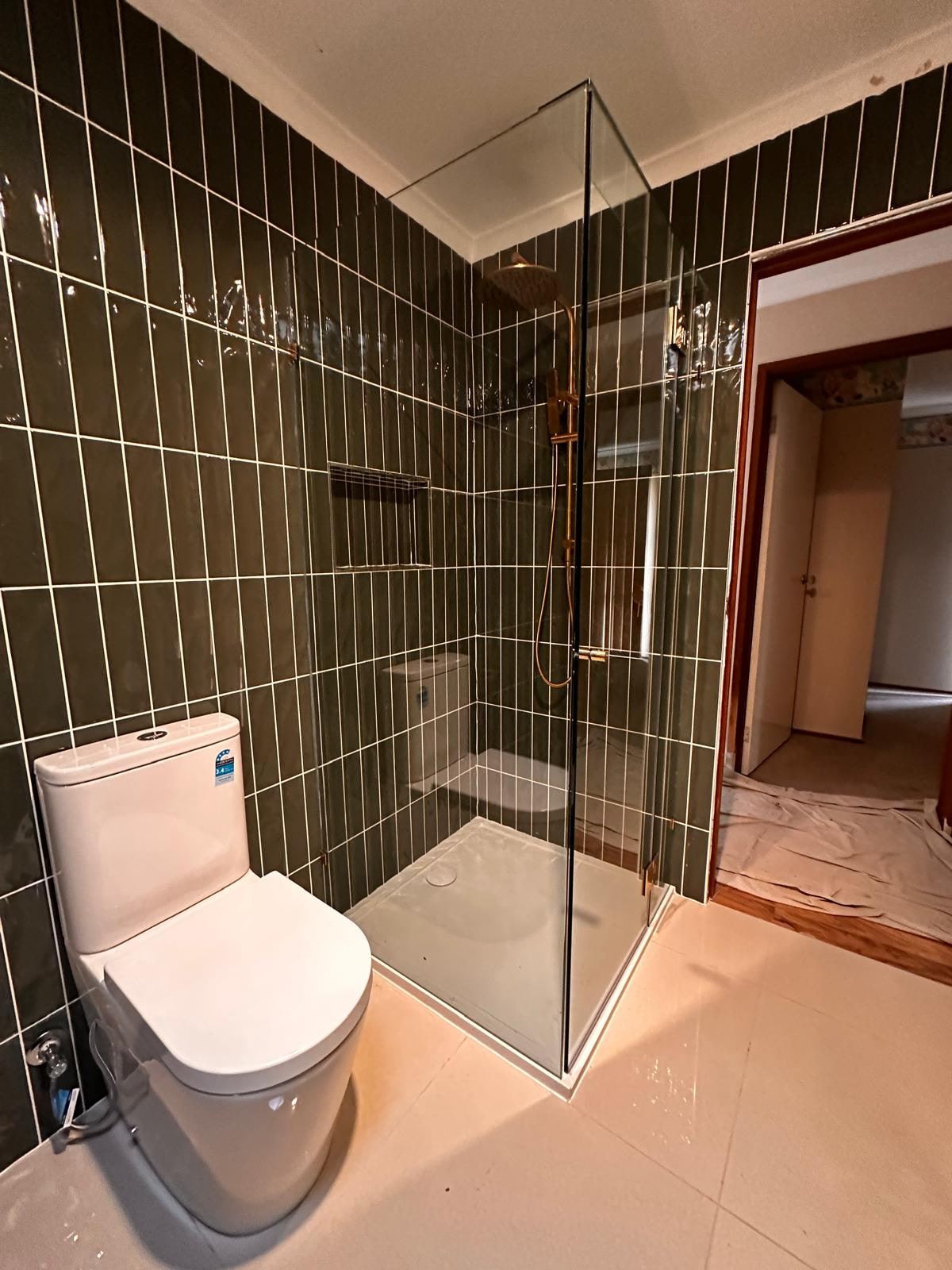 Frameless shower lined with deep green vertical tiles and brass fittings