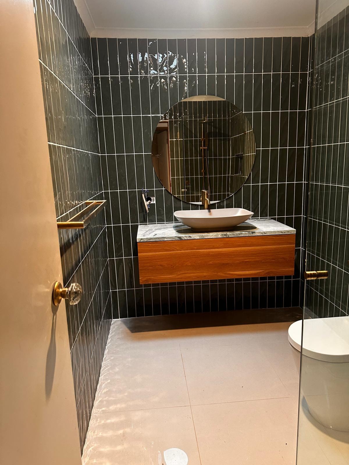 Renovated bathroom with deep green vertical tiles, round mirror, floating timber vanity and brushed brass tapware