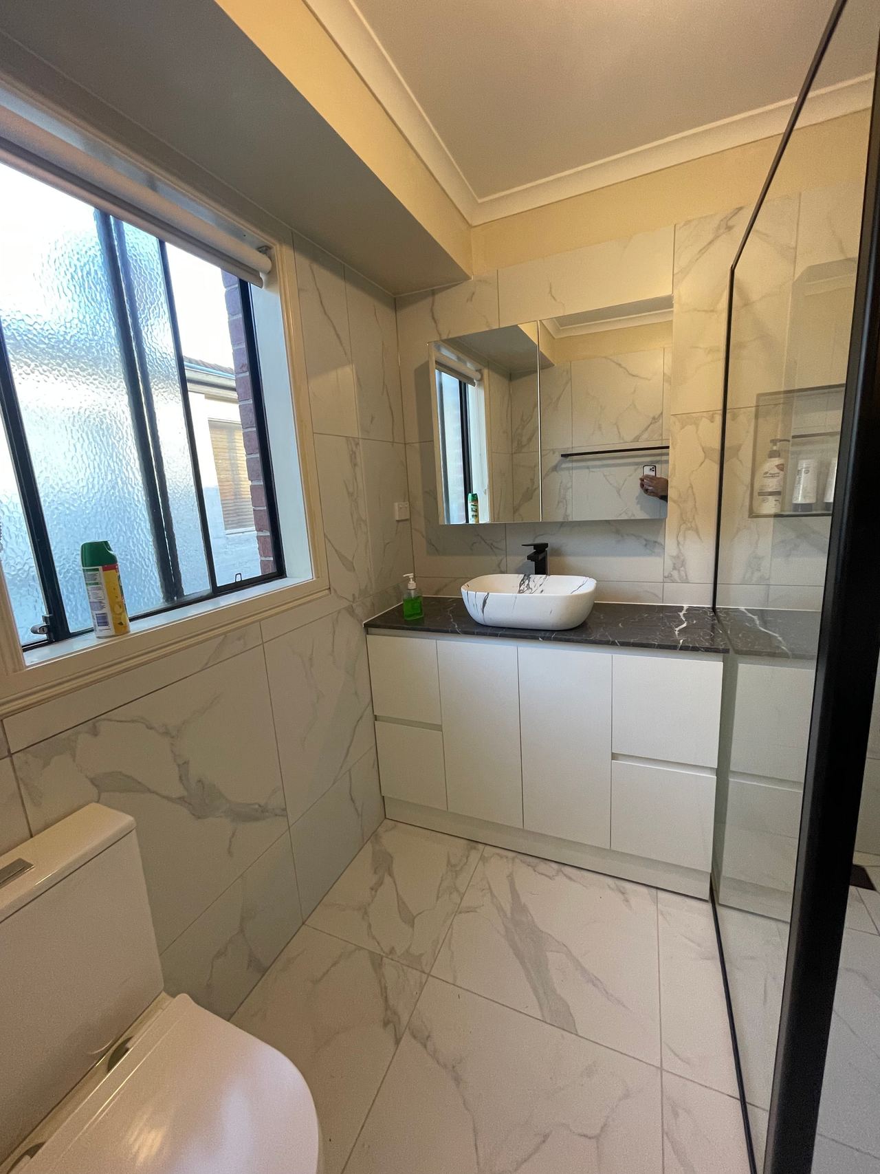 After: the same bathroom with marble-look tiles, a new vanity and black-framed shower