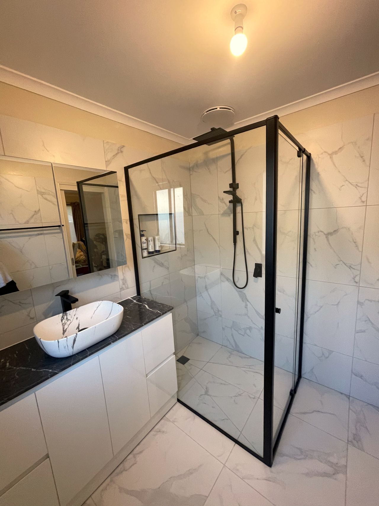 Renovated bathroom with marble-look tiles, a black-framed shower, mirror cabinet and vessel basin on a dark stone top