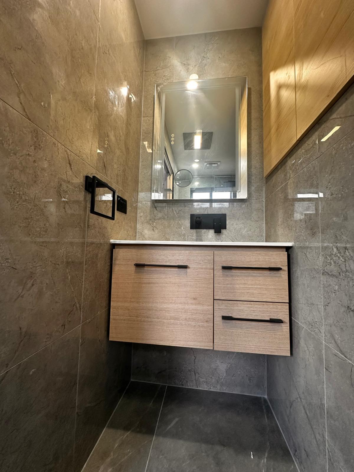 Wall-hung timber vanity with black handles, framed mirror and dark stone-look tiles