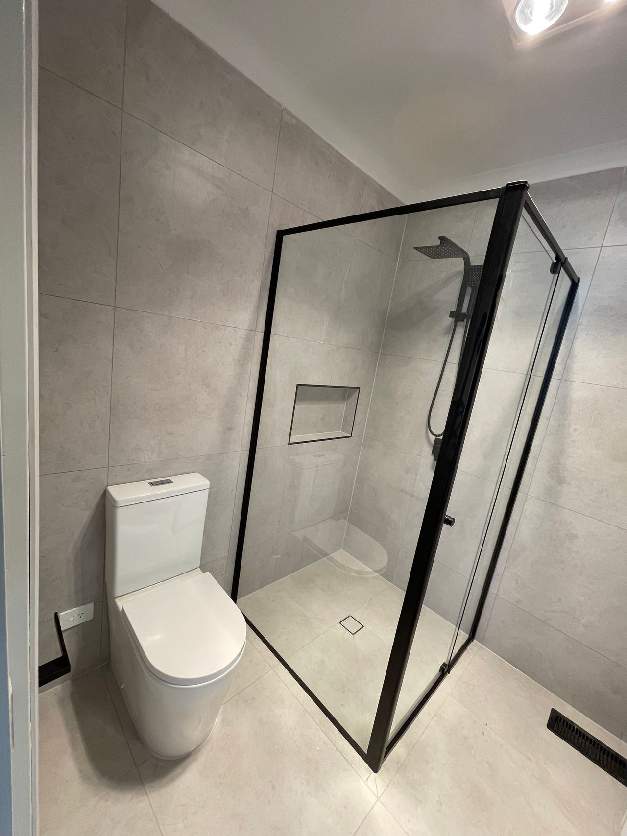 After: the same corner of the Mitcham bathroom with a black-framed shower, wall-faced toilet and full-height grey tiles