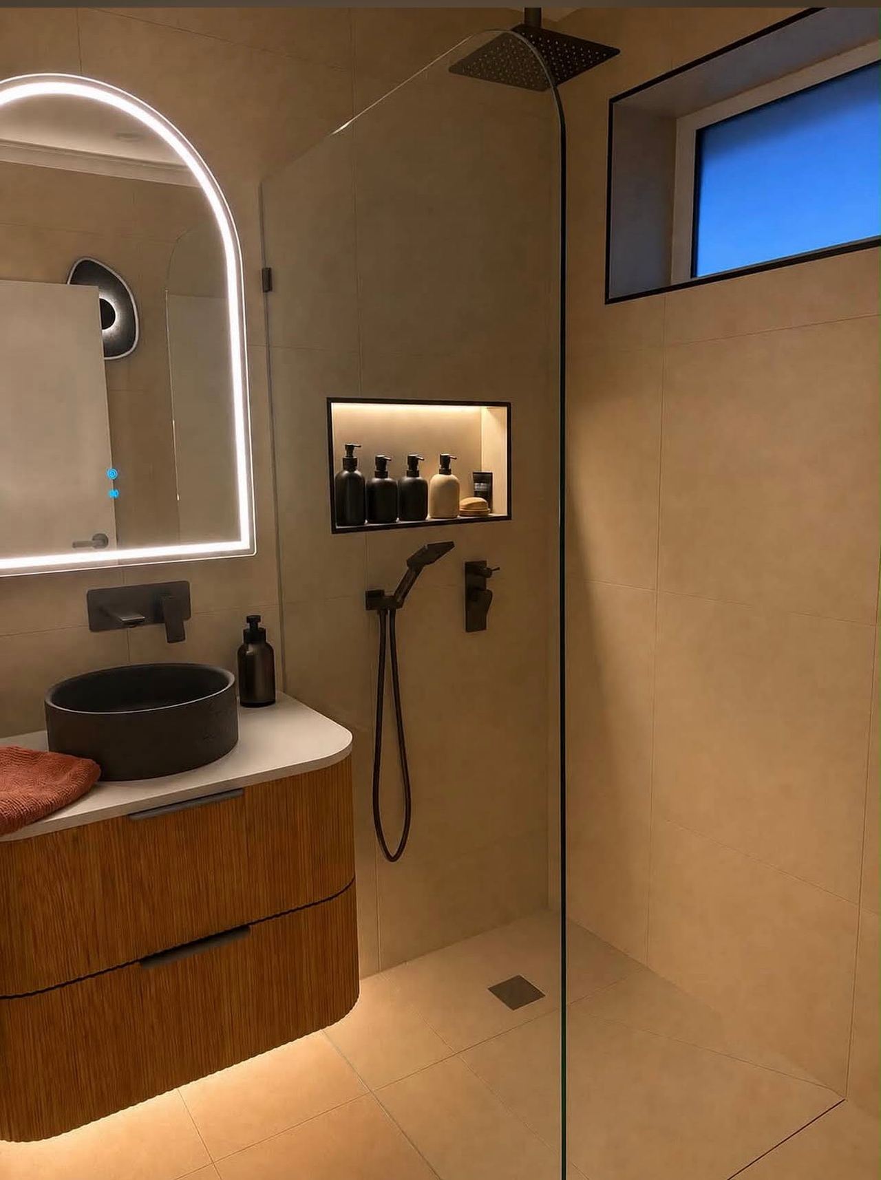 Renovated bathroom with a curved fluted timber vanity, stone basin, arched backlit mirror and lit shower niche