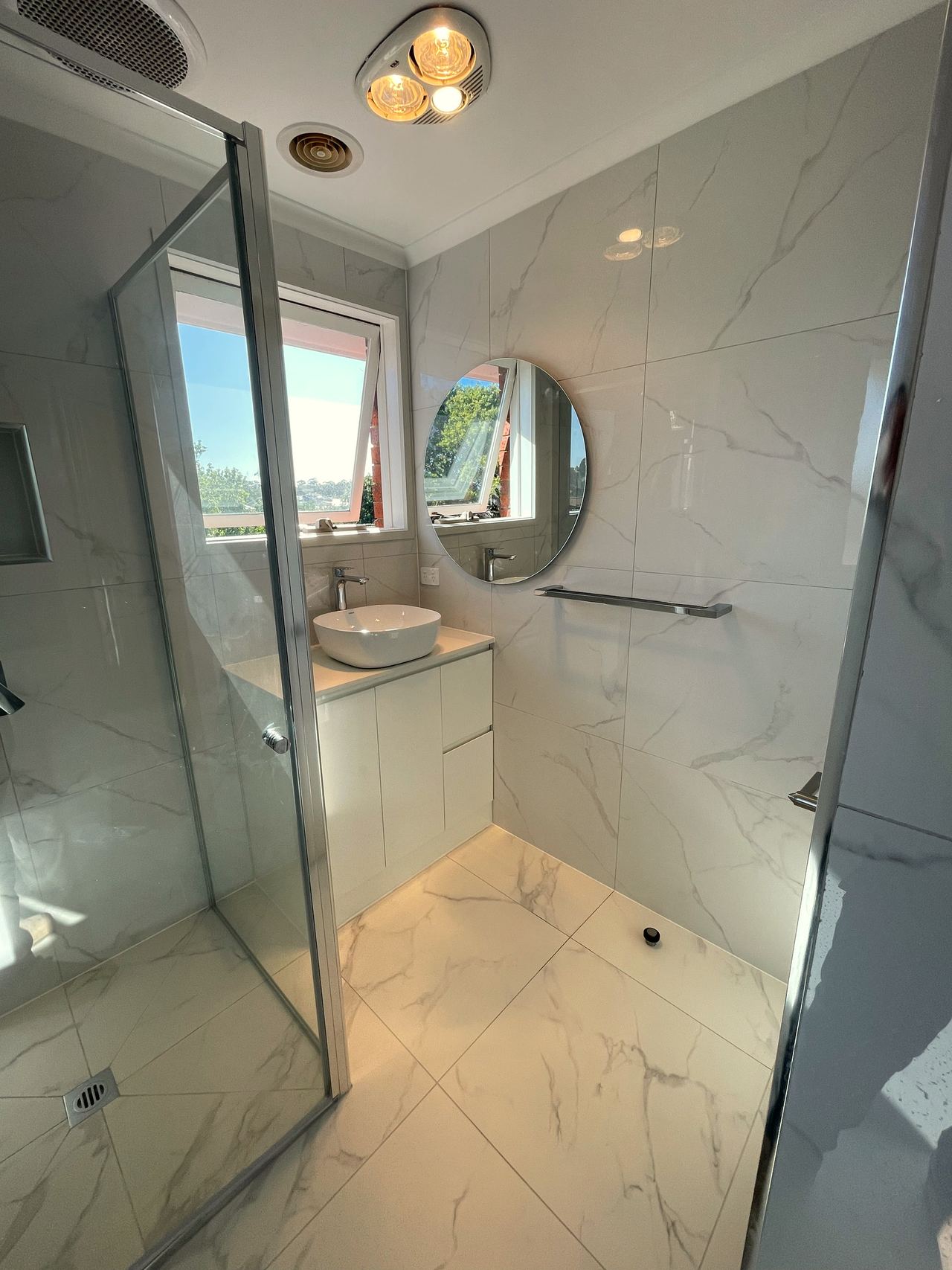 Renovated bathroom in Noble Park North with a frameless shower, round mirror and marble-look tiles