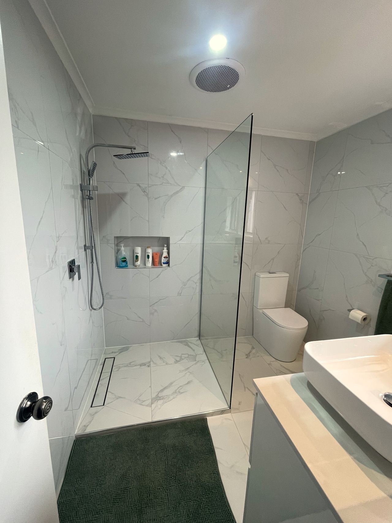 After: frameless walk-in shower beside a white vanity with marble-look tiles in Noble Park