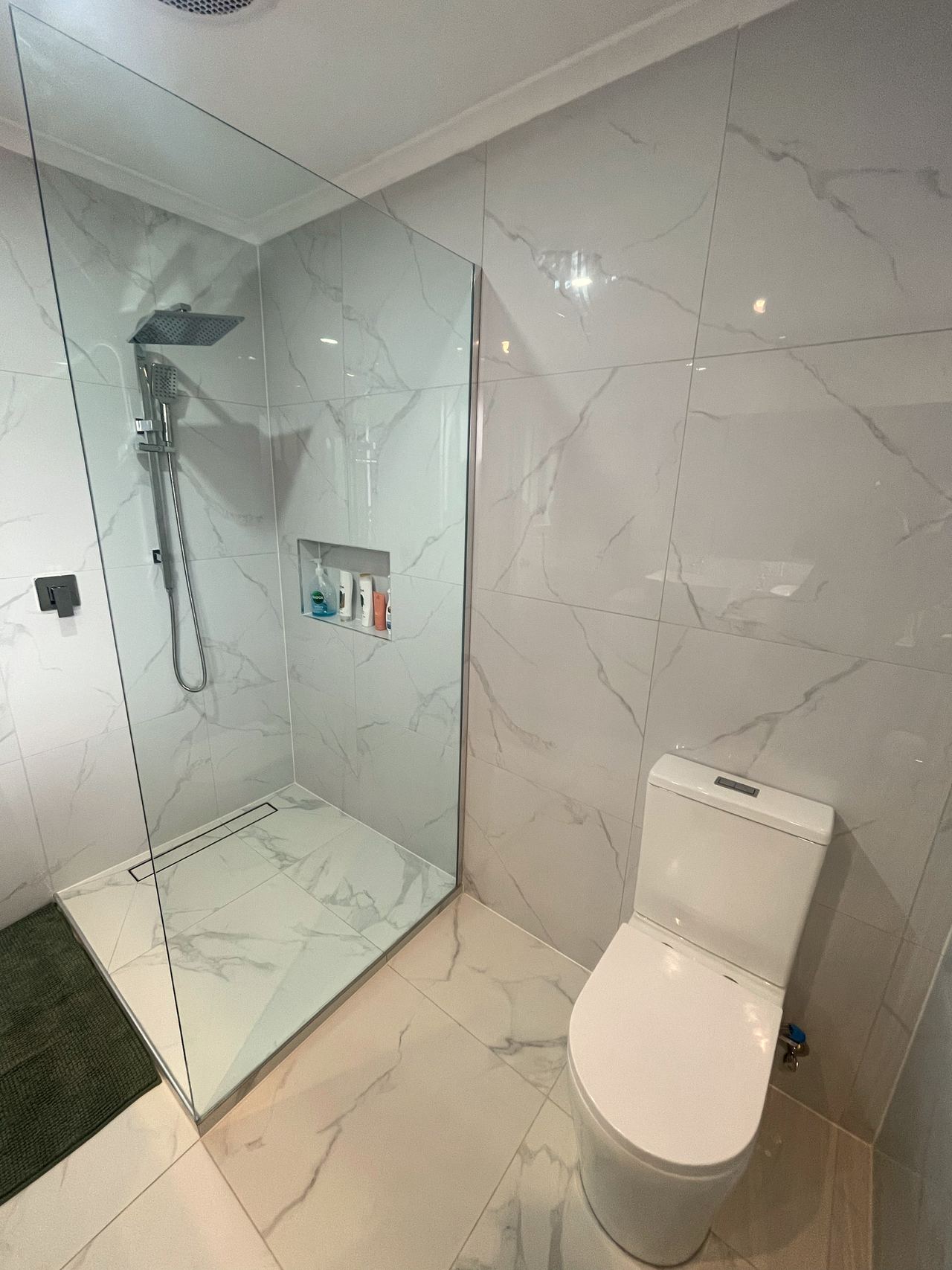 Walk-in shower with single glass panel, linear floor drain and wall niche in Noble Park