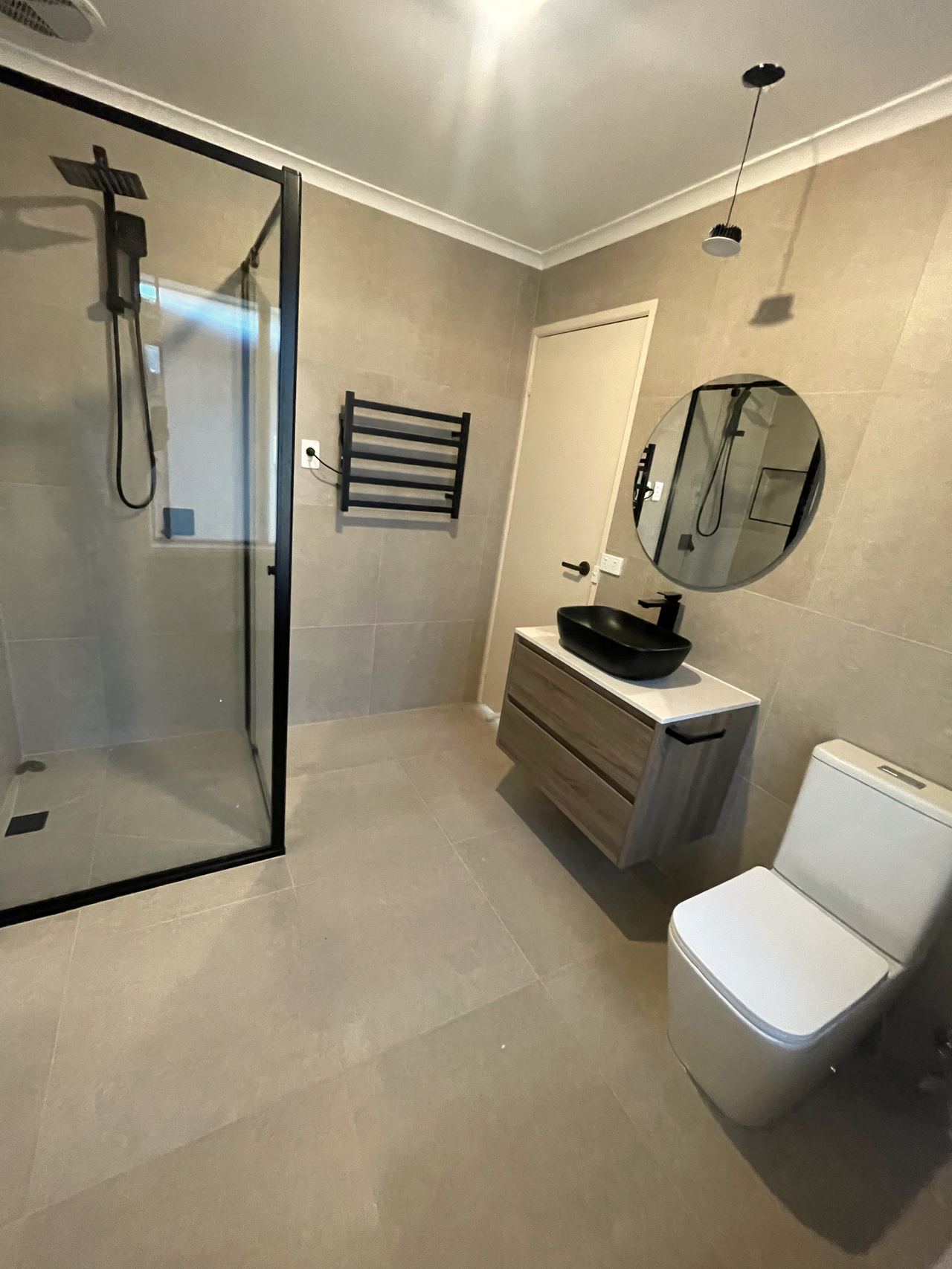 After: the same Rowville bathroom with a black-framed shower, round mirror, floating vanity with black vessel basin and heated towel rail