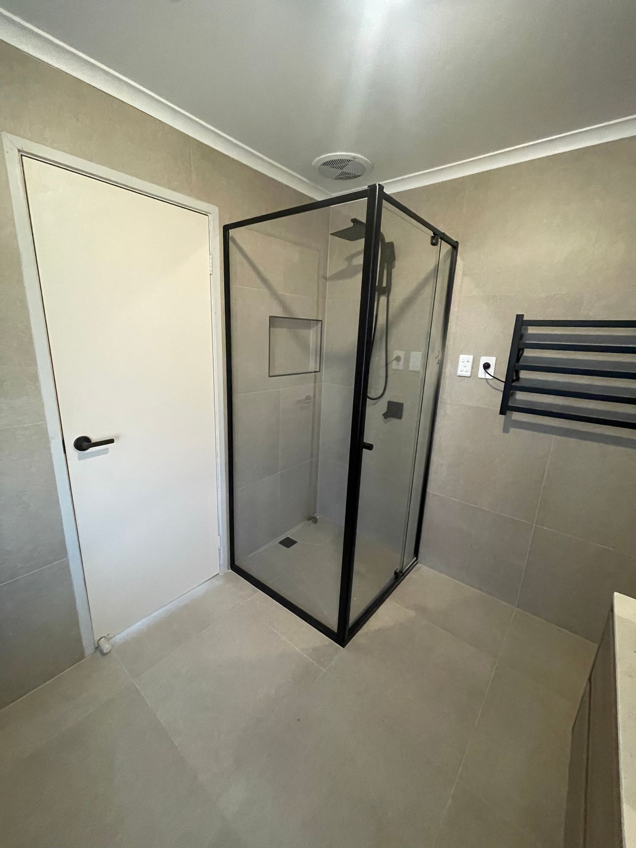After: black-framed corner shower and heated towel rail with large-format grey tiles in Rowville